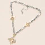 A silver and gold-tone necklace featuring a large four-petal flower pendant with iridescent white inlay, accented by two smaller matching flower charms on a silver chain, displayed on a light beige background.