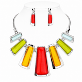 A statement necklace and matching drop earrings displayed on a white mannequin bust. The necklace features a silver-tone collar with multiple rectangular glass panels in red, yellow, lime green, and pale blue, arranged in a fan shape.