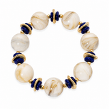 A beaded stretch bracelet featuring large cream and white marbled round beads, deep blue cylindrical beads, and textured gold-toned spacer rings, shown on a plain white background.