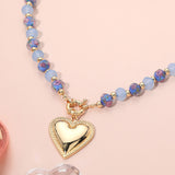 Necklace with blue beads and a gold heart pendant on a pink background