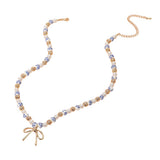 Blue floral ceramic bead necklace featuring pearls, gold accents, and a delicate gold bow pendant on a white background