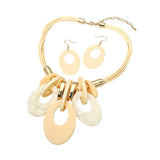 A gold-tone statement necklace with matching drop earrings, featuring multiple layered circular and oval charms in cream and pale peach tones on a white background.