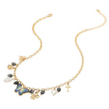Gold charm station necklace featuring a colorful enamel butterfly, pearl, heart, flower, bow and cross charms with decorative black bead accents on a white background 