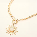 Gold celestial sunburst pendant necklace with white opal-inspired center and modern link chain on a light beige background