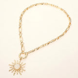 Gold celestial sunburst pendant necklace with white opal-inspired center and modern link chain on a light beige background