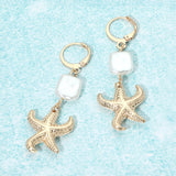 Gold coastal starfish charm drop huggie earrings with square pearl accents and lightweight beach-inspired design.