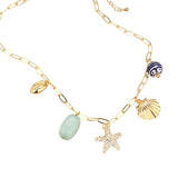 Gold coastal charm necklace with pavé starfish, shell charms, natural stone and patterned bead. Gold necklace with various charms including a starfish, shell, and bead on a white background. 