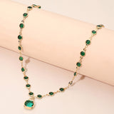 Emerald green crystal bezel station necklace with cushion cut pendant displayed on cream cylindrical stand