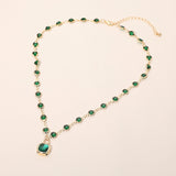 Emerald green crystal round bezel station necklace with square pendant silver tone on cream background