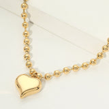 Gold beaded necklace with a heart pendant on a white background