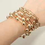Seven-piece gold stretch bracelet set featuring polished geometric ball and bar bead designs for a modern layered look with a plain background