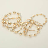 Seven-piece gold stretch bracelet set featuring polished geometric ball and bar bead designs for a modern layered look on a light beige background