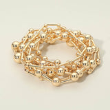 Seven-piece gold stretch bracelet set featuring polished geometric ball and bar bead designs for a modern layered look on a beige background