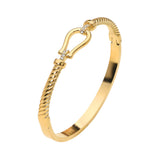 Gold stainless steel twisted hinged bangle bracelet with horsebit buckle accent and crystal details on a white background