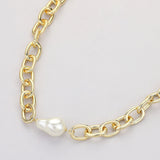 Chunky gold link chain necklace with baroque pearl detail close up on grey background