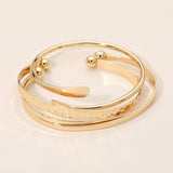 Three-piece gold dipped minimalist bracelet set featuring layered bangles and open cuff designs for elegant everyday styling on a beige background