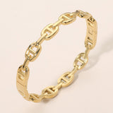 Gold stainless steel modern link hinged bangle bracelet featuring polished elongated chain links and a secure hinged closure on a beige background