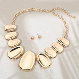 Gold necklace and earrings on a textured beige surface