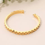 Gold stainless steel textured chain link hinged bangle bracelet featuring a dimensional chain-inspired edge and polished finish on a beige background