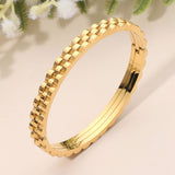 Gold stainless steel textured chain link hinged bangle bracelet featuring a dimensional chain-inspired edge and polished finish on a beige background