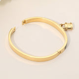 Turquoise enamel hinged bangle bracelet with gold-tone stainless steel finish and lock charm accent on a beige background