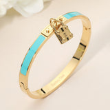 Turquoise enamel hinged bangle bracelet with gold-tone stainless steel finish and lock charm accent on beige background