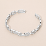 A polished silver chain link bracelet with a unique geometric interlocking design, displayed on a solid light beige background.