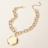 Gold chunky chain necklace with organic round plate pendant and modern statement design on a light beige background