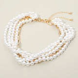 Close up detail of multi-strand simulated pearl choker with gold tone wire accents on cream background