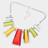 A silver-tone geometric statement necklace featuring six elongated, fan-shaped resin cabochons in red, yellow, and light green, suspended from a silver snake chain against a light gray background.