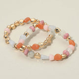 Two-piece stretch bracelet set featuring multicolor pebble-shaped beads and polished gold-tone accents in a layered design on a beige background