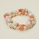 Two-piece stretch bracelet set featuring multicolor pebble-shaped beads and polished gold-tone accents in a layered design on a beige background