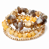 A stack of five beaded stretch bracelets featuring a mix of polished gold-tone beads, smooth yellow-orange beads, and natural agate stones in earthy brown, gray, and cream tones, set against a plain white background.