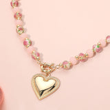 Necklace with pink beads and a gold heart pendant on a pink background