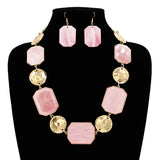 Pink geometric resin and hammered gold disc statement necklace and earring set displayed on black jewelry bust