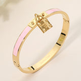 Pink enamel hinged bangle bracelet with gold-tone stainless steel finish and lock charm accent on a beige background