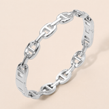 A polished silver chain link bracelet with a distinctive interlocking link design, displayed on a soft beige background.