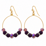 A pair of gold hoop earrings with faceted purple beads and iridescent pink and purple accent beads, shown on a plain white background.
