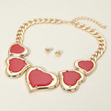 Gold necklace with red heart pendants on a beige background