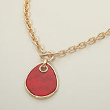 Gold necklace with a red pendant on a light beige background
