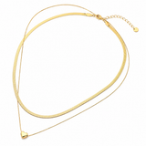 A double-layered gold chain necklace featuring a thick textured snake-style top layer and a delicate fine chain bottom layer with a small heart-shaped pendant, displayed on a clean white background.
