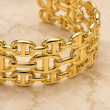 A close-up of a gold-tone chain-link bracelet resting on a light beige marble surface.