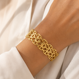 A close-up of a gold chain link bracelet worn on a person's wrist, styled with a white blouse.