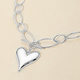 A silver heart pendant necklace with a matching link chain, displayed on a light beige background.