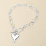 A silver-toned chain bracelet with elongated oval links and a heart-shaped charm, displayed on a solid beige background.