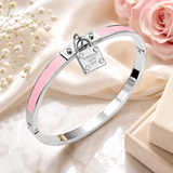 Silver stainless steel hinged bangle bracelet featuring pink enamel inlays and a decorative lock charm with polished finish on a beige background.
