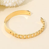 Gold-tone stainless steel sculptural interlock hinged bangle bracelet featuring chain-inspired detailing and a polished modern design on a beige background
