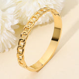 Gold-tone stainless steel chain accent hinged bangle bracelet featuring a modern chain link design and polished finish on a beige background