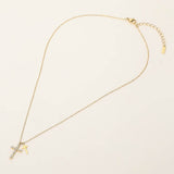 Gold stainless steel double cross pendant necklace with crystal cross charm on a delicate chain on a light beige background
