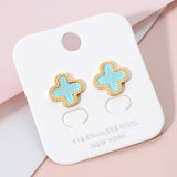 Gold stainless steel quatrefoil stud earrings with glossy turquoise stone center on pink background